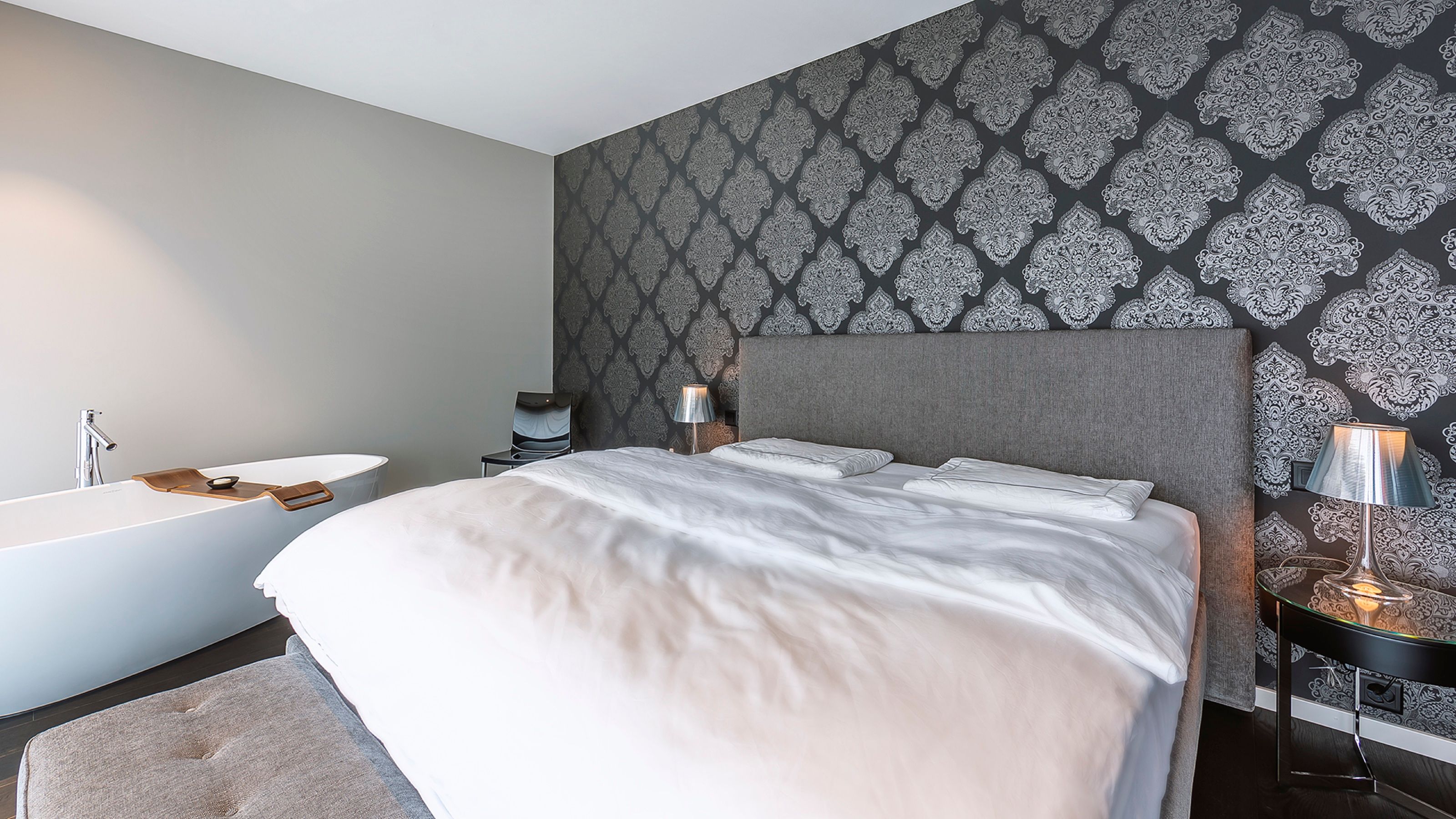 Schlafzimmer mit gepolstertem Kopfteil vor Ornamenttapete